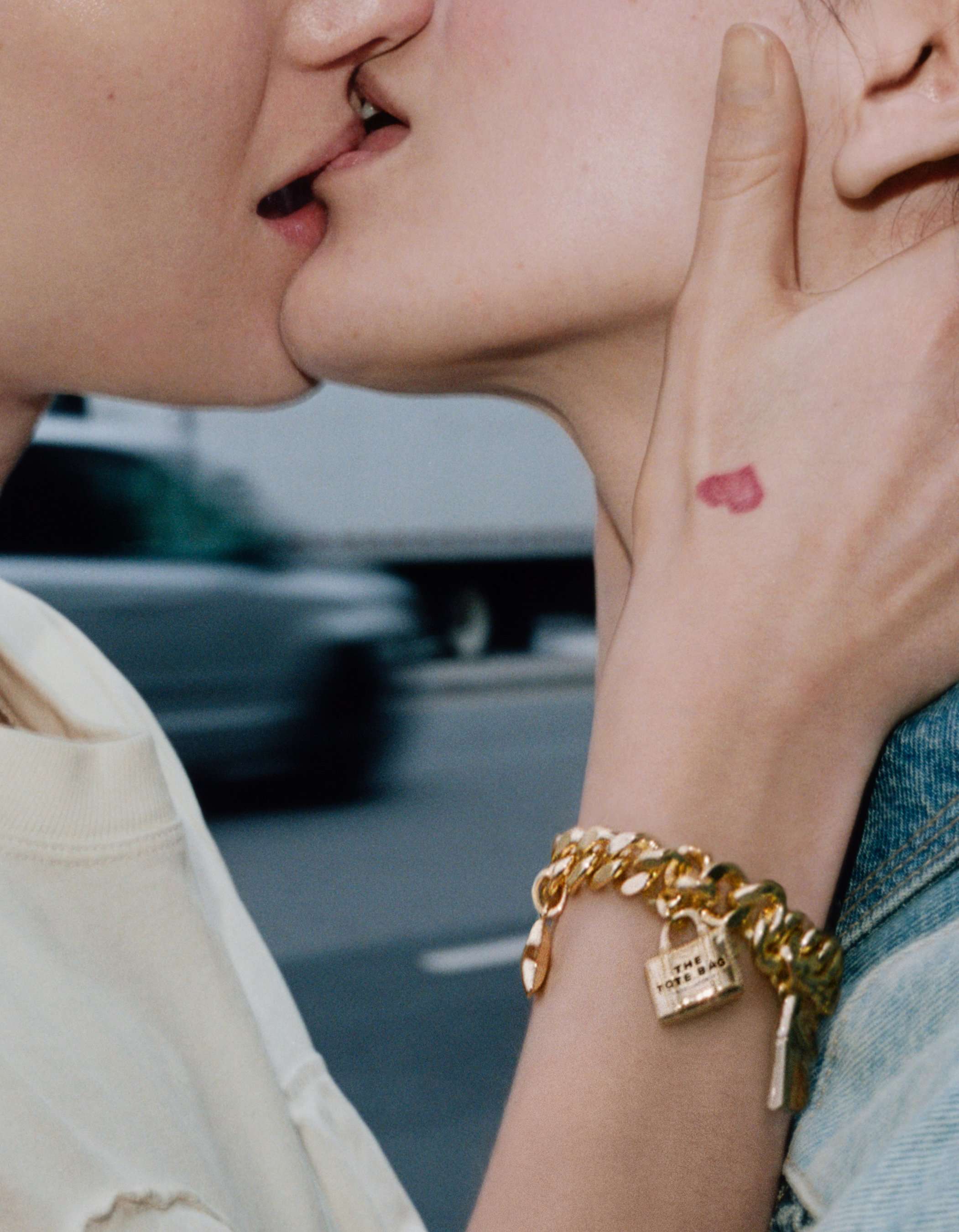 Two women kissing, with one of them wearing The Mini Icon Charm Bracelet in Light Antique Gold on her wrist.